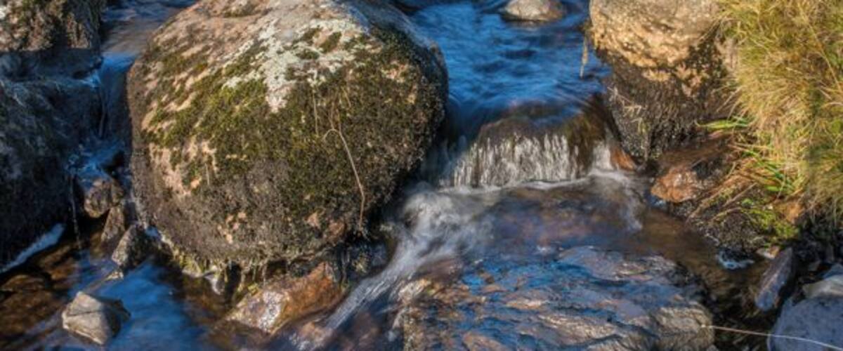 A stream flowing over rocks with a stone bridge in the background.