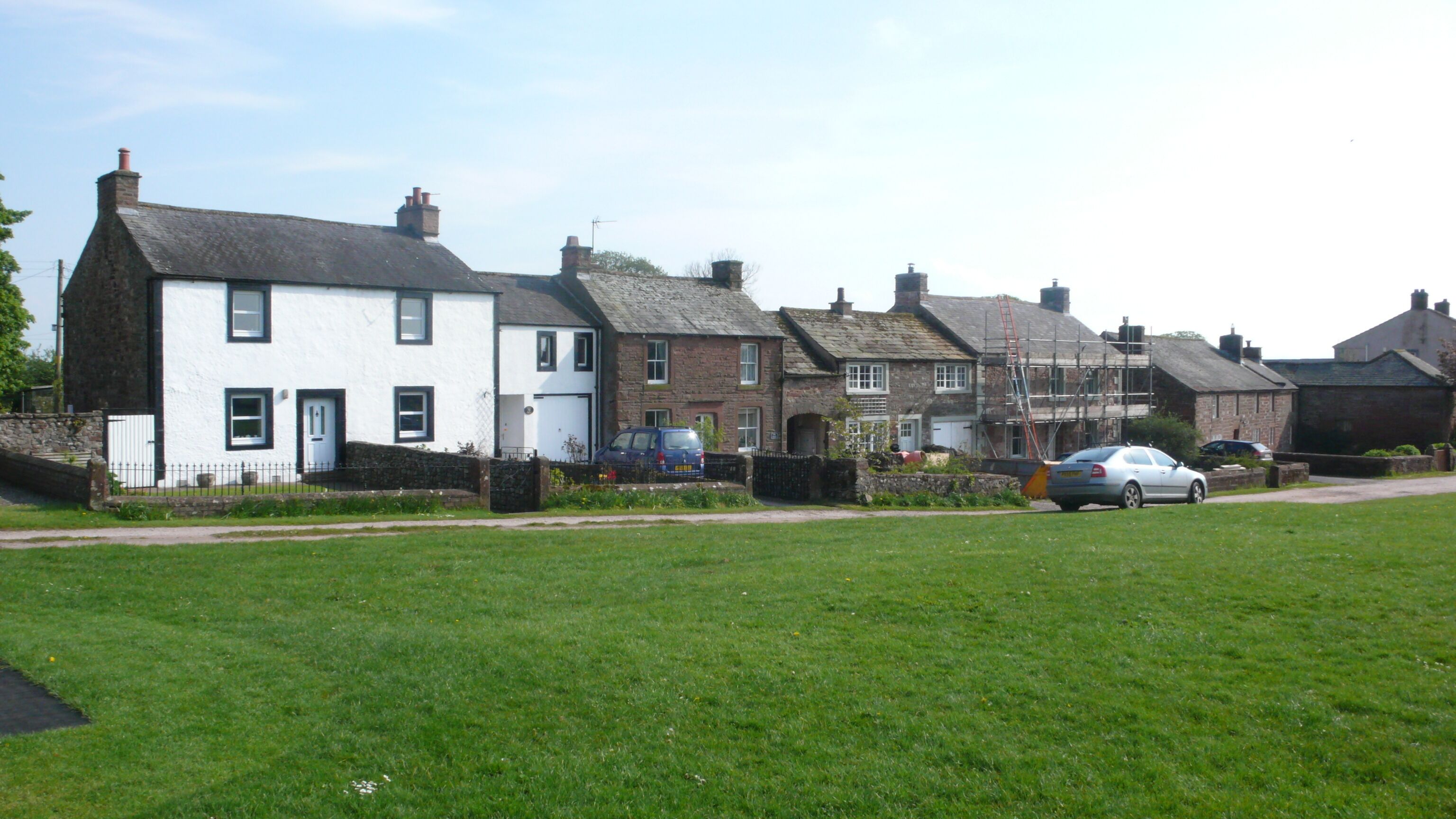 A row of white and brick houses with a grassy field in the foreground.