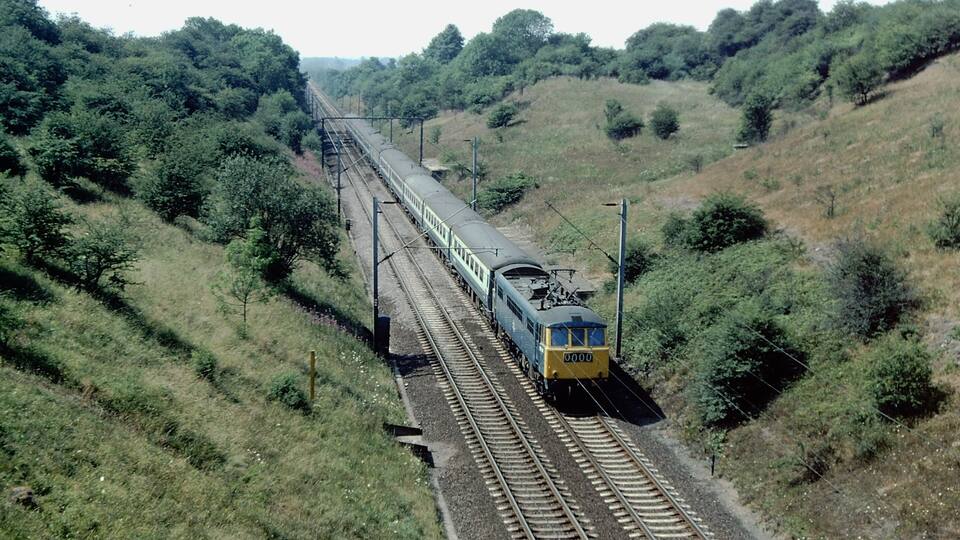 A train on a railway track surrounded by lush greenery and hills.
