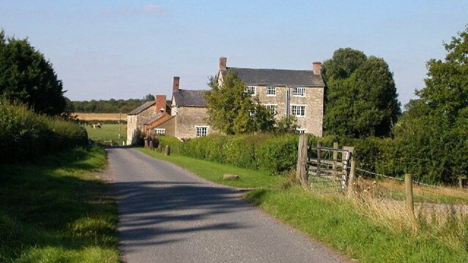 A rural road flanked by stone houses and lush greenery.