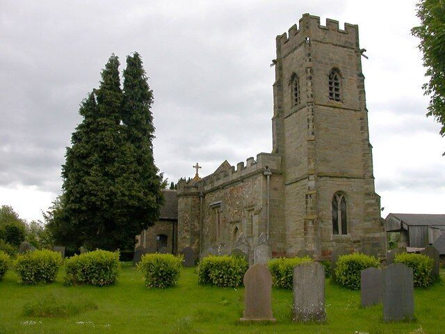 A historic church with a tall tower and a large tree in the foreground.