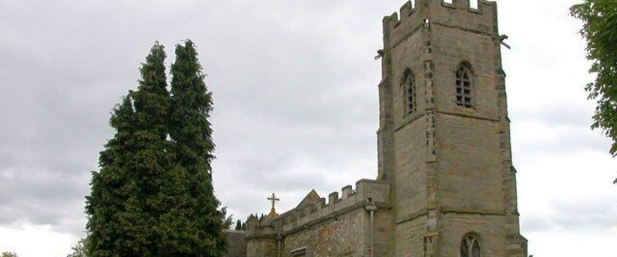 A historic church with a tall tower and a large tree in the foreground.