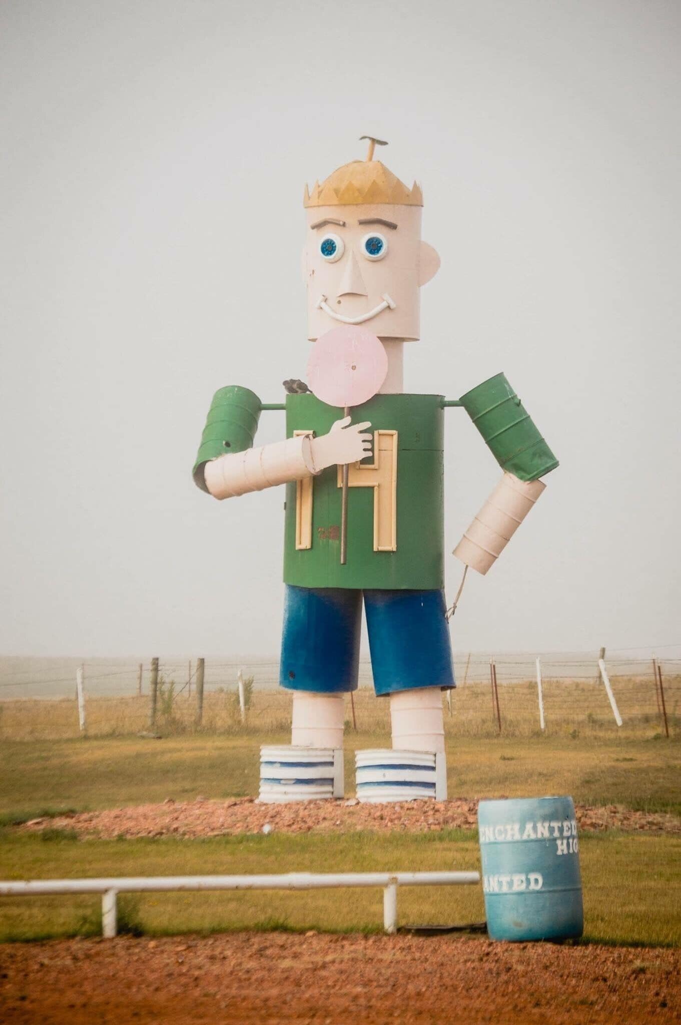 A large cardboard cutout of a character holding a pink object, standing next to a barrel labeled "ENCHANTED HIDDEN".