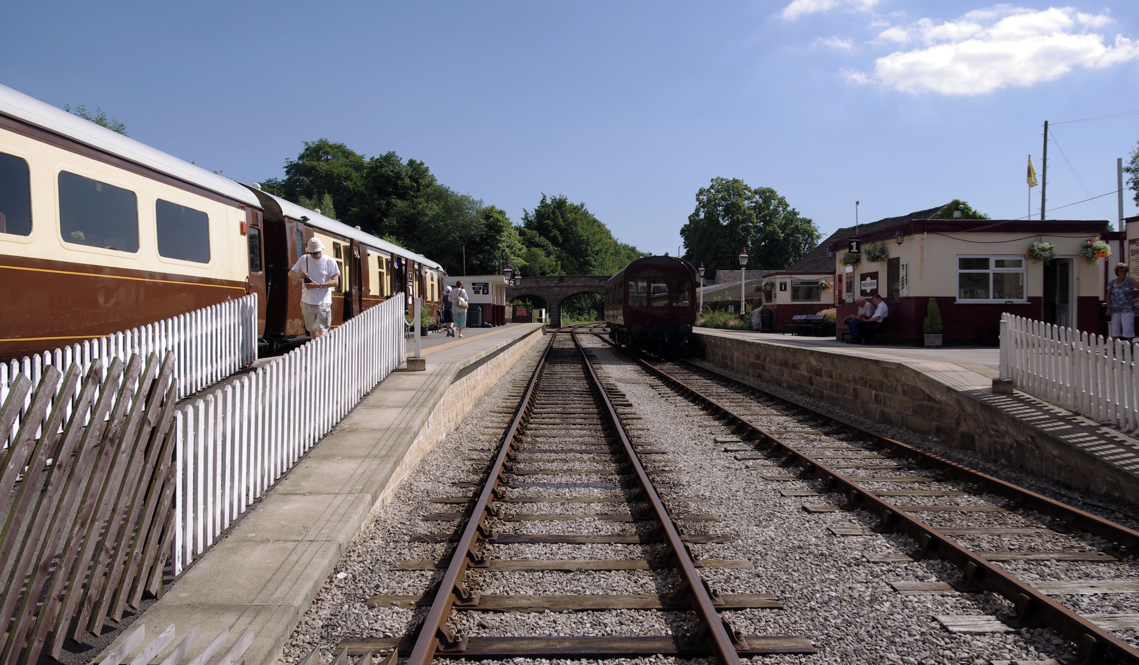 A railway station with two tracks, a platform, and a white fence.