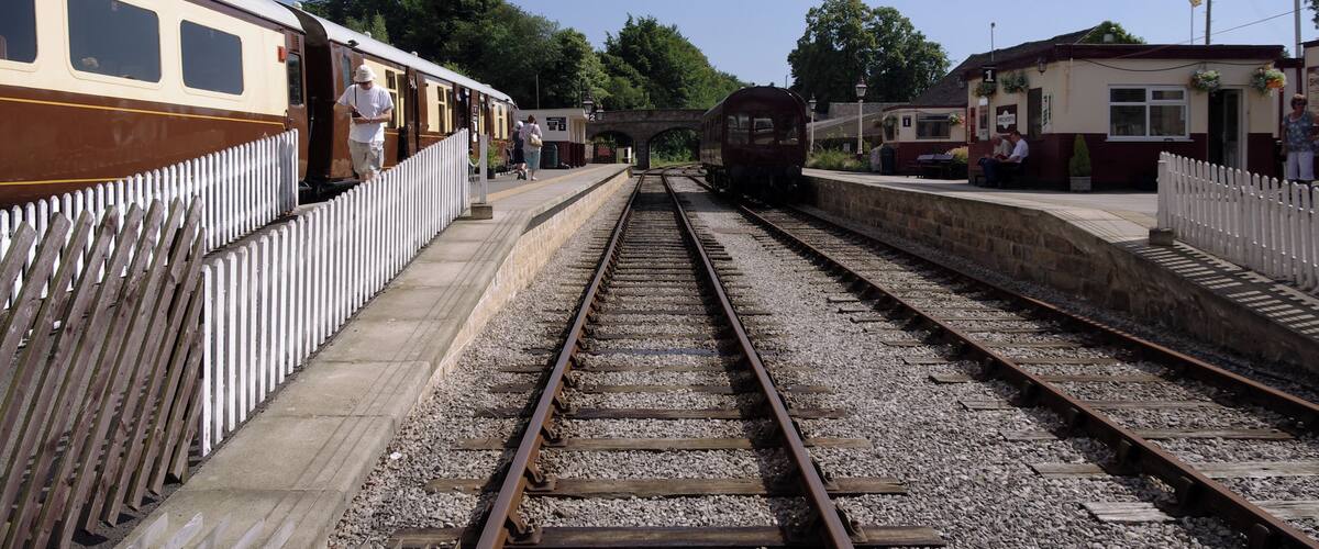 A railway station with two tracks, a platform, and a white fence.