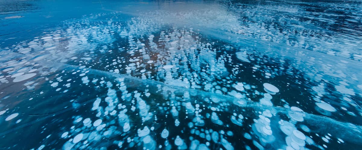 A frozen lake with ice floes, mountains in the background, and a clear sky.
