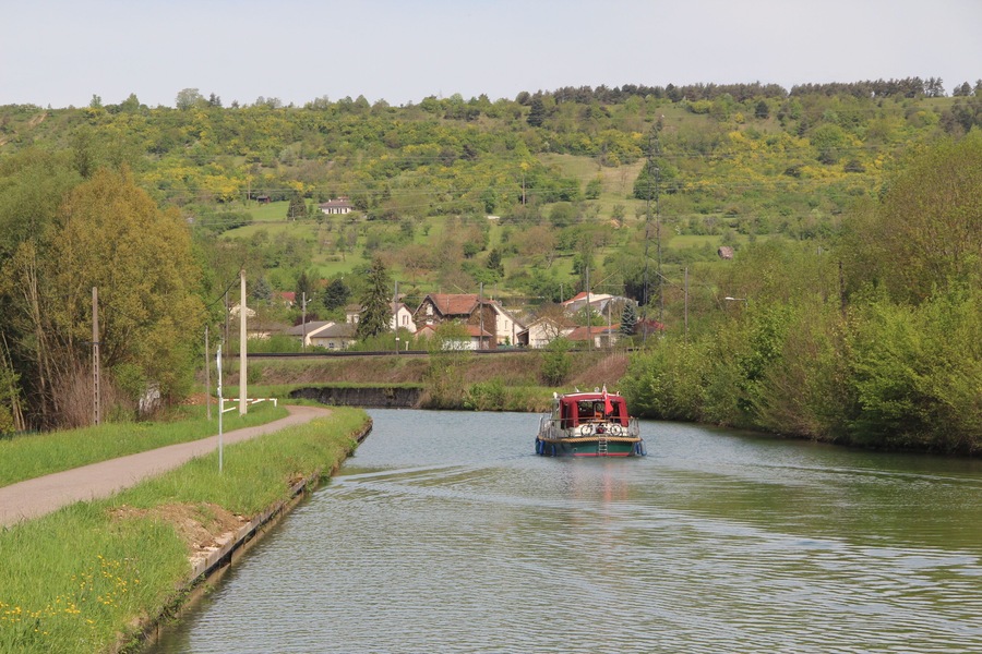 A narrow waterway with a boat, surrounded by lush greenery and houses in the background.