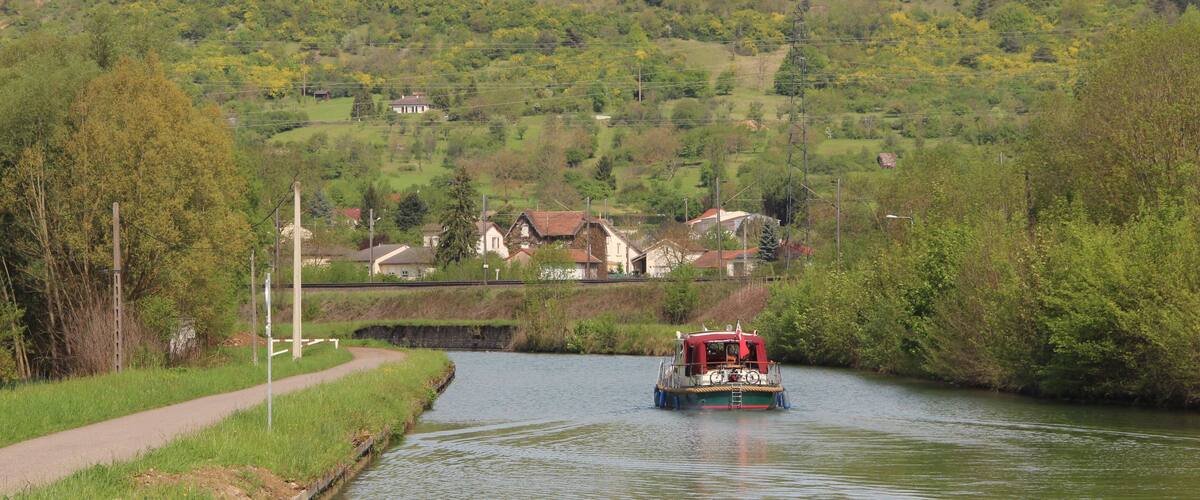 A narrow waterway with a boat, surrounded by lush greenery and houses in the background.