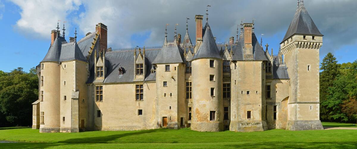 A large, historic castle with multiple towers and turrets, surrounded by lush green lawns.
