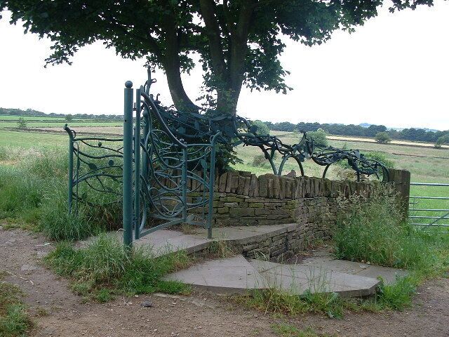 A metal gate with a stone wall and steps leading to a grassy field.
