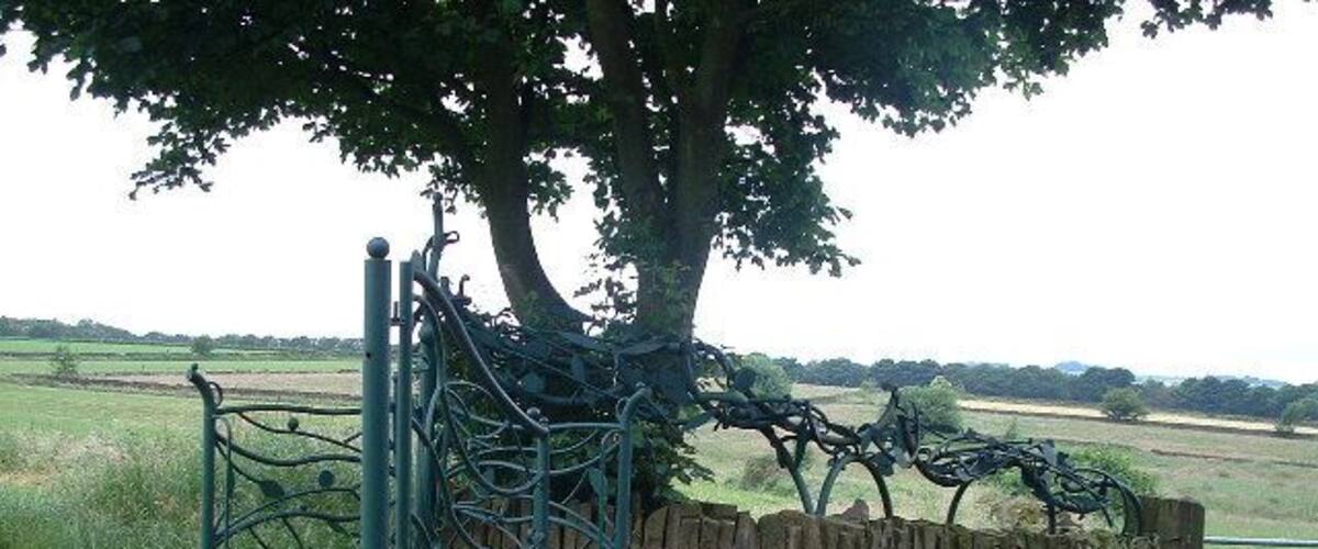 A metal gate with a stone wall and steps leading to a grassy field.