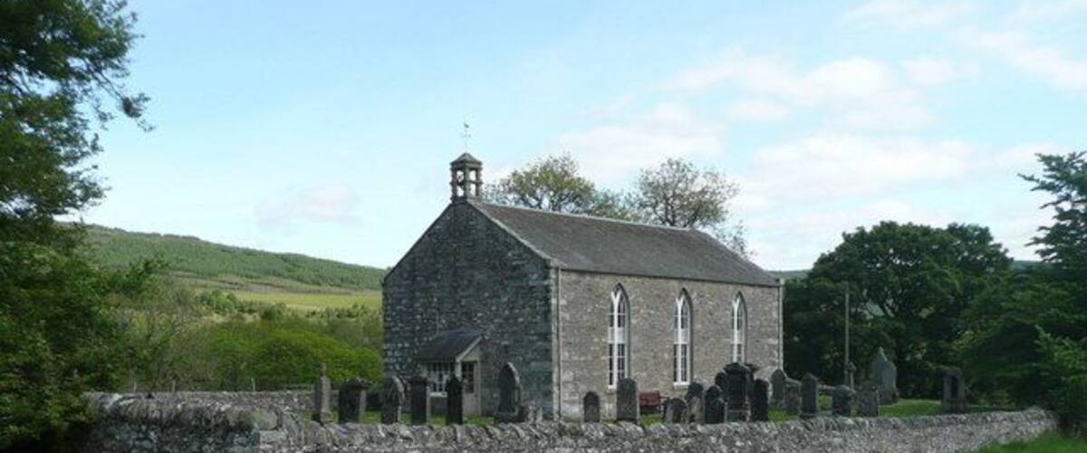 A stone church with a bell tower, surrounded by a stone wall and a grassy field.
