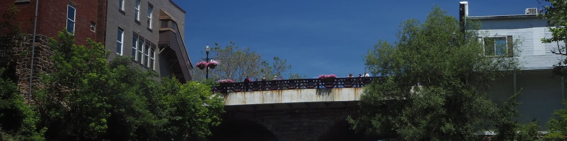 A waterfall under a bridge with buildings on either side.