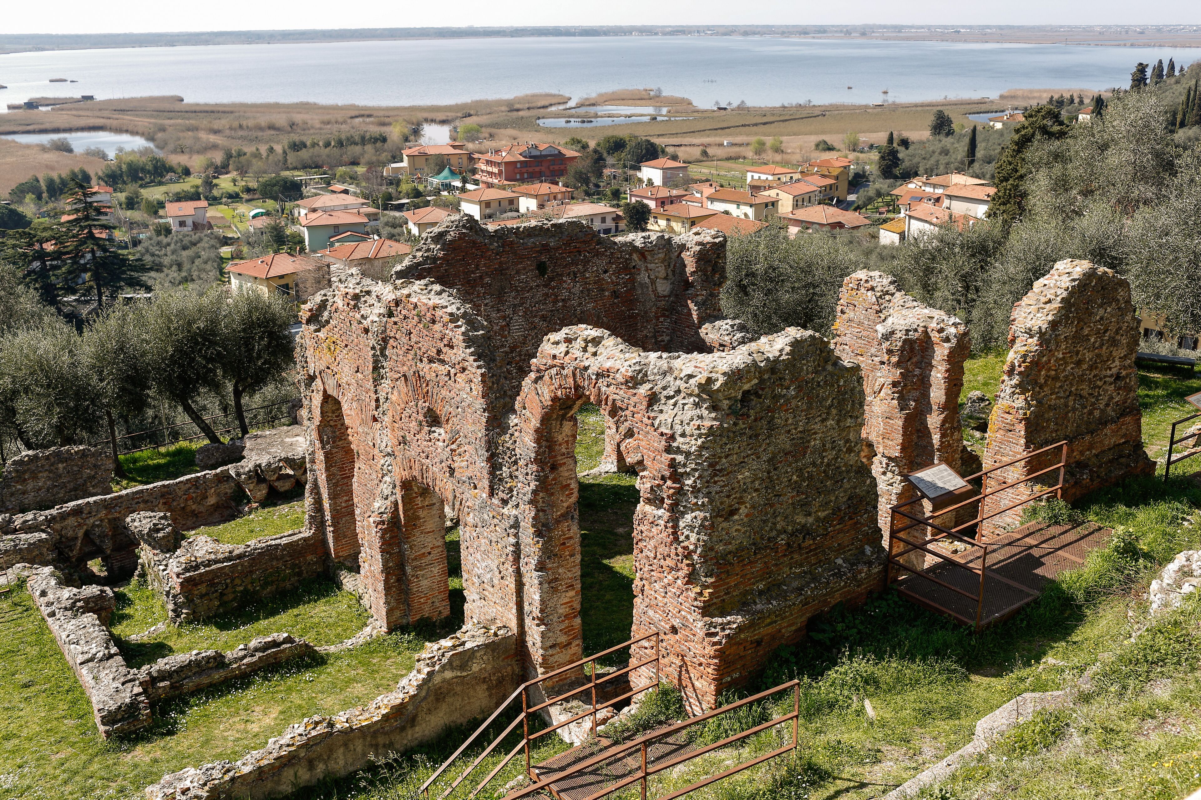 Ancient ruins with a town in the background and a lake.