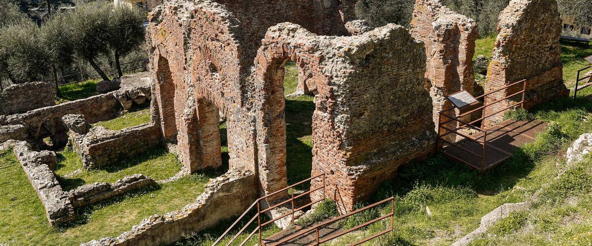 Ancient ruins with a town in the background and a lake.
