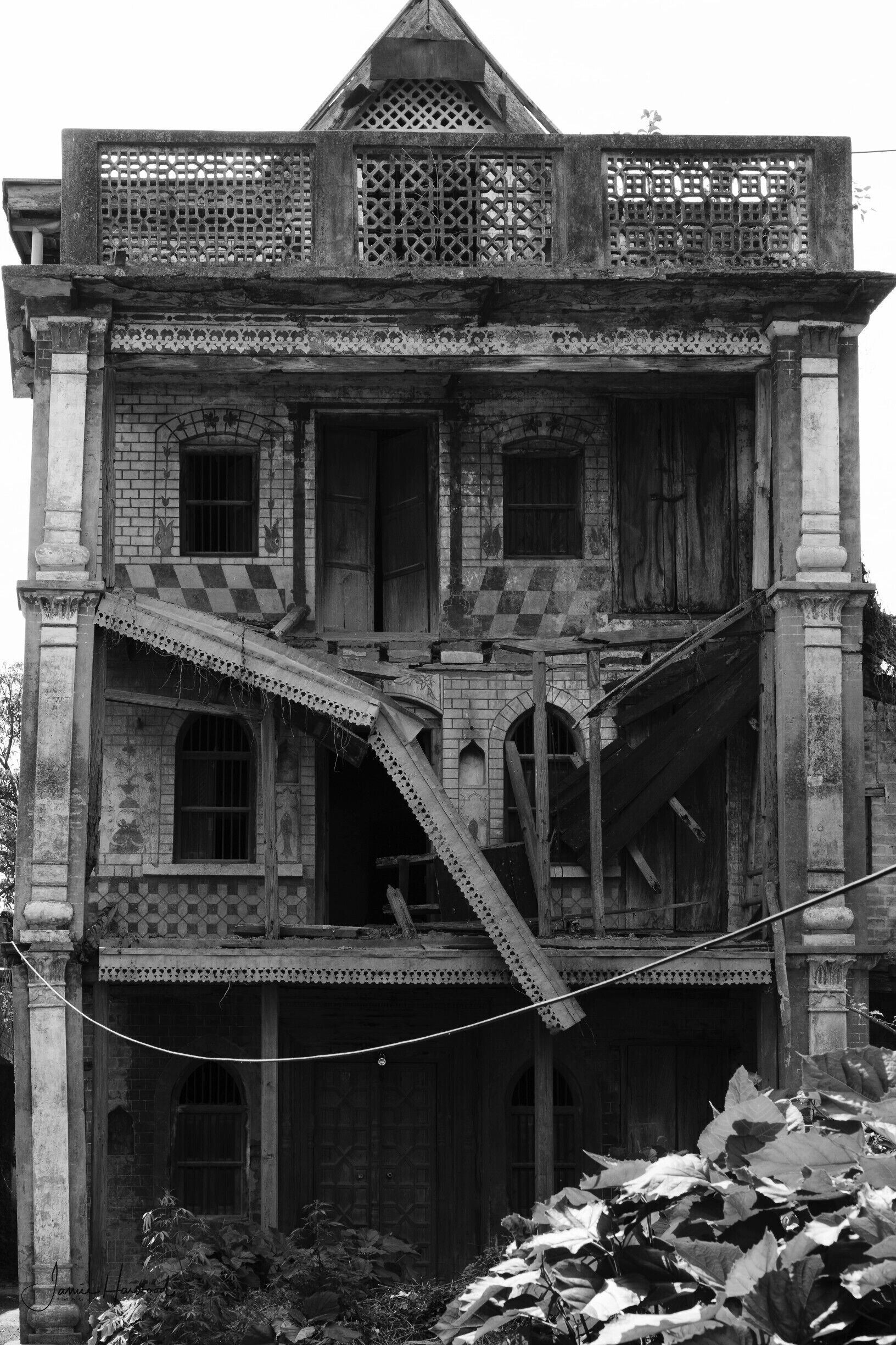 A large, ornate building with intricate architectural details, including a balcony with latticework and a staircase leading to the upper floor.
