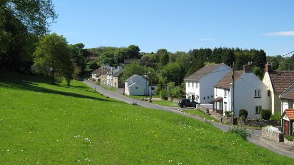 Une colline verdoyante, avec une route qui mène à une rangée de maisons blanches aux toits bruns.