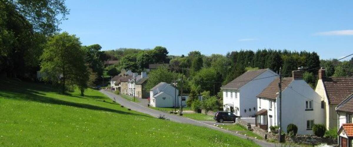 A green hillside with a road leading to a row of white houses with brown roofs.