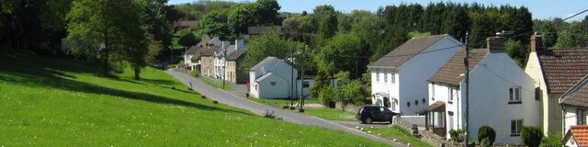A green hillside with a road leading to a row of white houses with brown roofs.