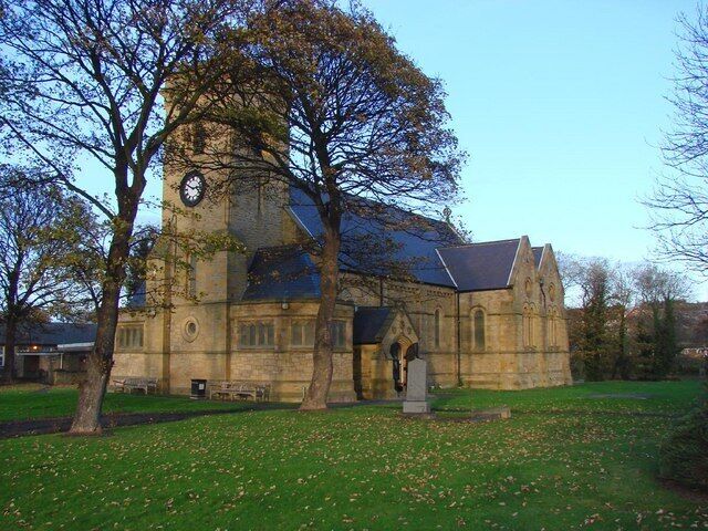 A historic stone church with a clock tower, surrounded by trees and a grassy lawn.
