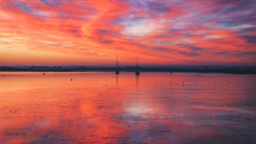 A sunset over a calm lake with boats and a distant city skyline.