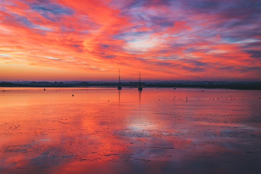 A sunset over a calm lake with boats and a distant city skyline.