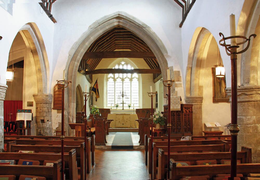 An interior of a church with wooden pews, a high arched ceiling, stained glass windows, and stone walls.