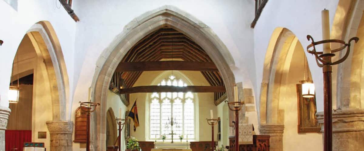 An interior of a church with wooden pews, a high arched ceiling, stained glass windows, and stone walls.