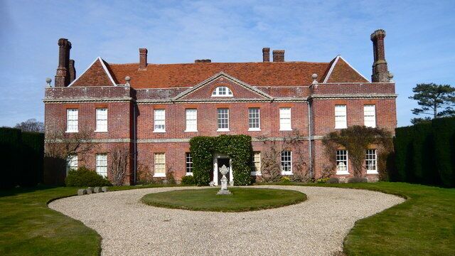 A large brick building with a symmetrical facade, a central entrance, and a gravel driveway leading to a circular lawn area.