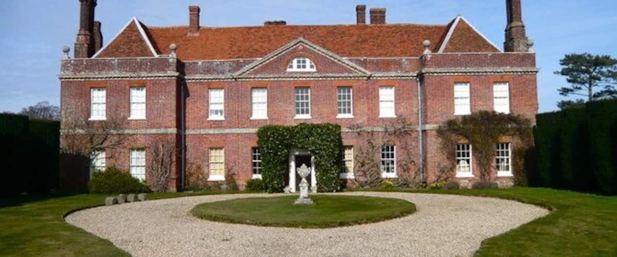 A large brick building with a symmetrical facade, a central entrance, and a gravel driveway leading to a circular lawn area.