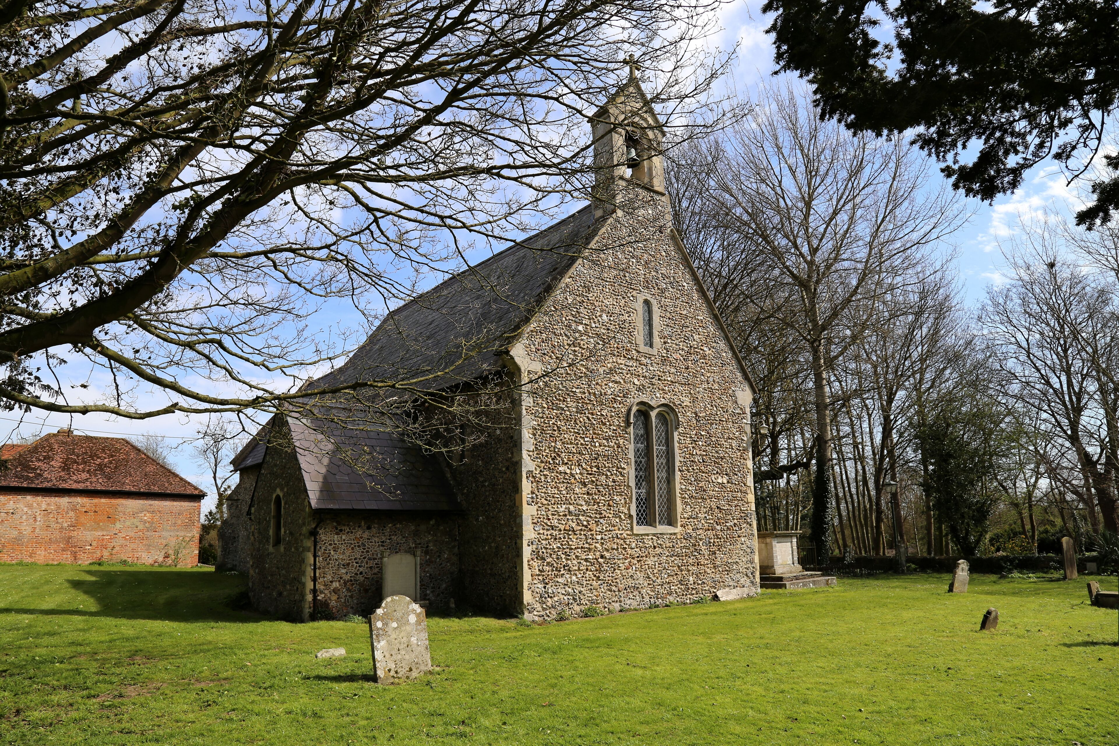 A small stone church with a bell tower, surrounded by a grassy cemetery with headstones.