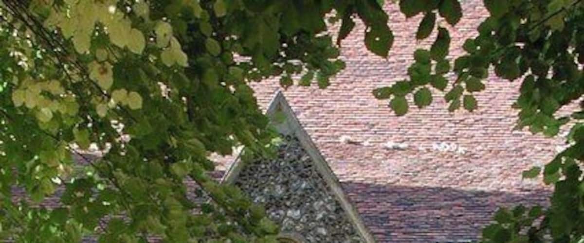 A stone church entrance with a pointed archway, a lantern above, and a brick building in the background.
