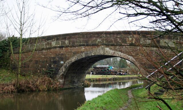 A stone bridge over a calm river with a grassy bank and bare trees.