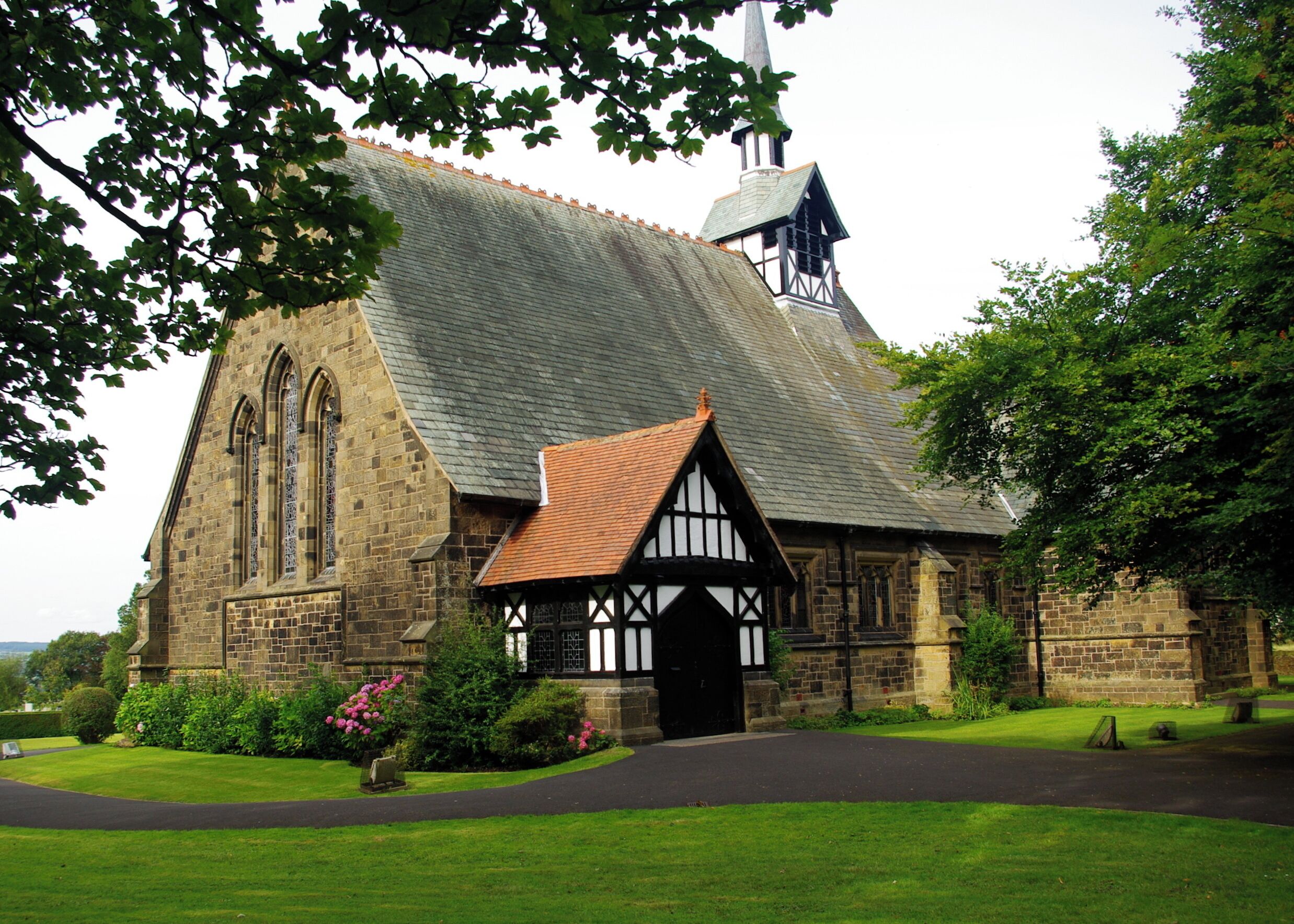A church with a steeply pitched roof, a prominent tower, and a small adjacent building with a tiled roof.