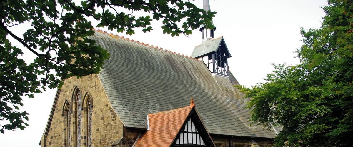 A church with a steeply pitched roof, a prominent tower, and a small adjacent building with a tiled roof.