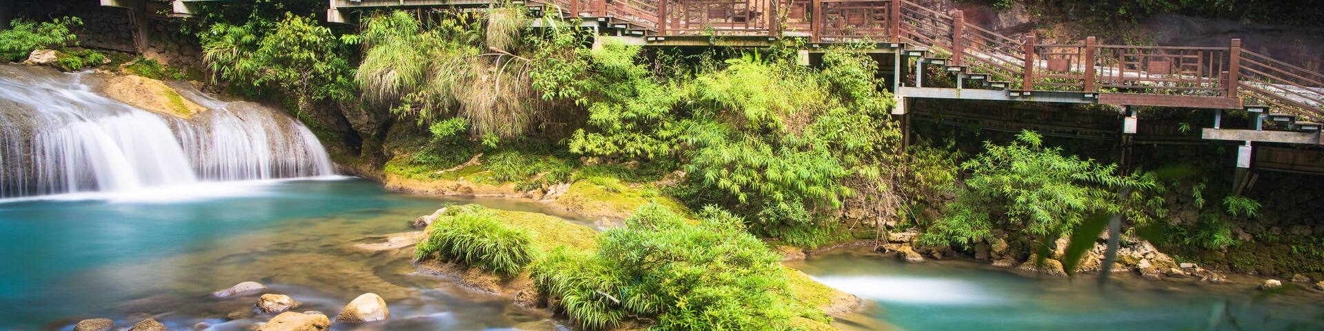 A waterfall, a bridge, and a river surrounded by lush greenery.