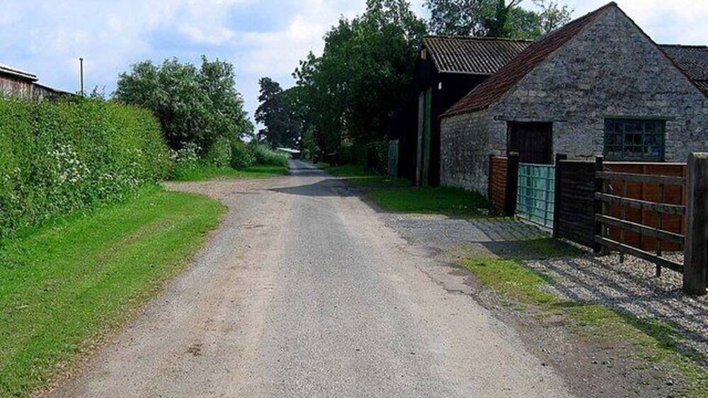 Eine Landstraße, die zu einem Steinhaus mit einem Metallgatter führt.