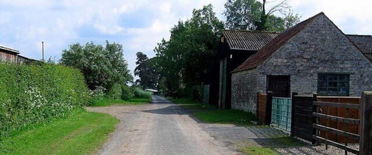 A rural road leading to a stone building with a metal gate.