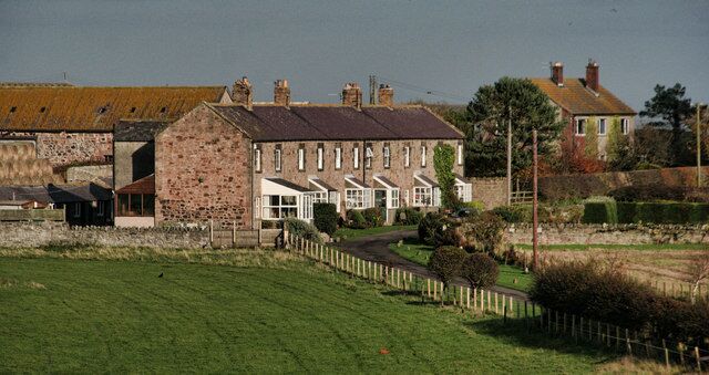 A stone building with a red roof, surrounded by a green field and a wooden fence.