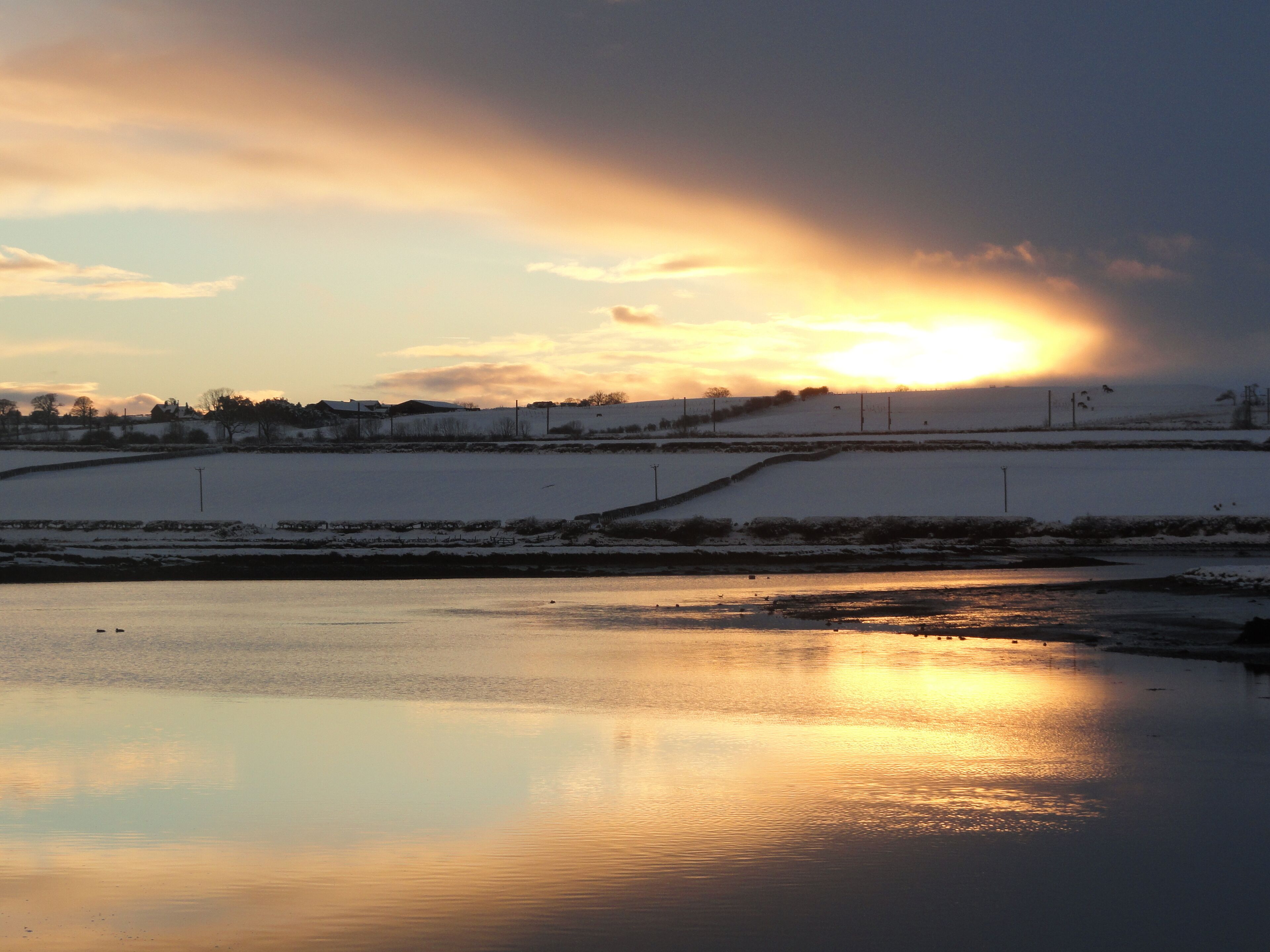 A frozen landscape with a sunset reflecting on the water.