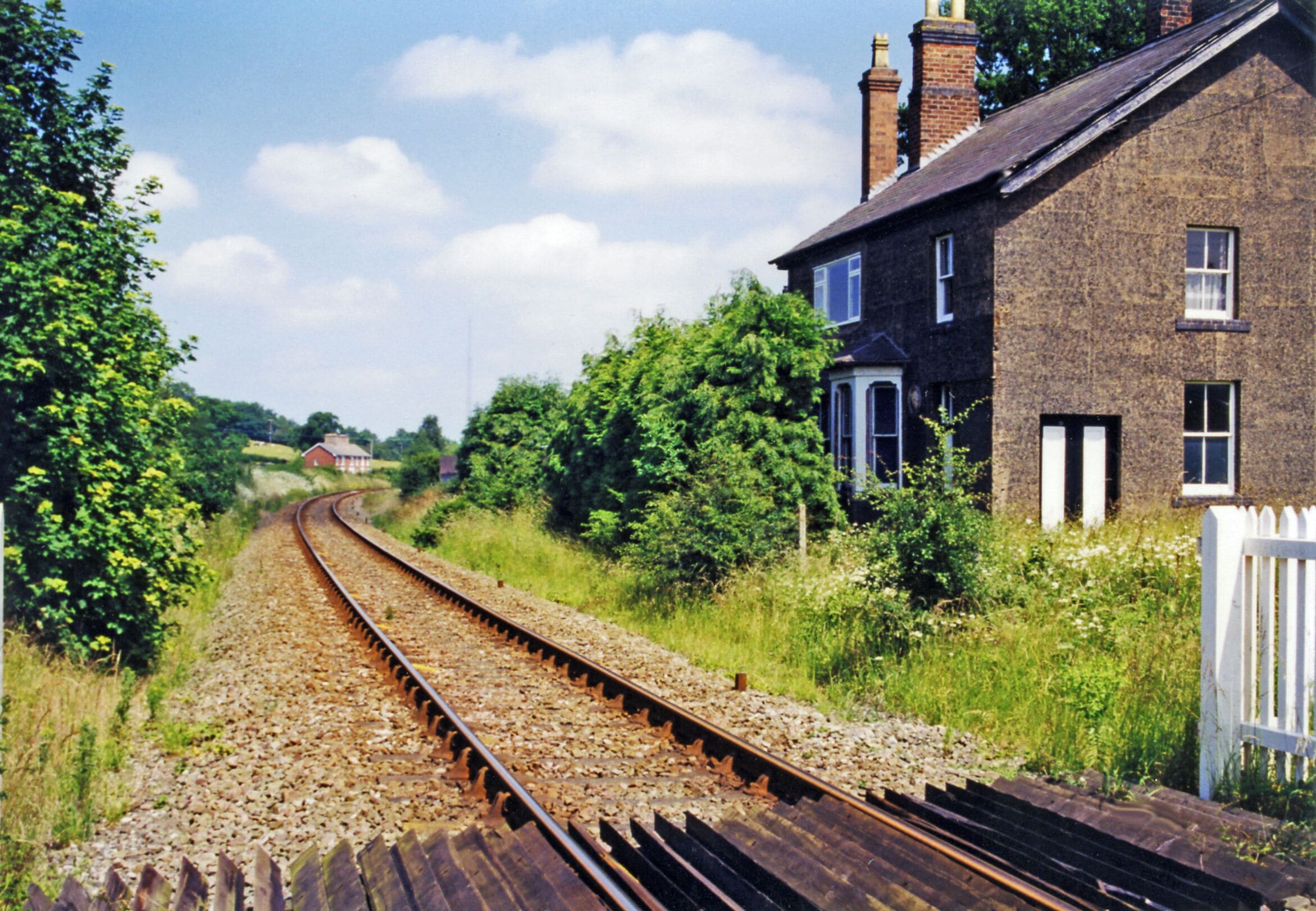 A railway track curving through a rural area with a brick house and greenery on the right.