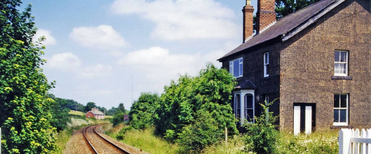 A railway track curving through a rural area with a brick house and greenery on the right.
