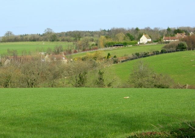 A rural landscape with green fields, a white house, and a fence.
