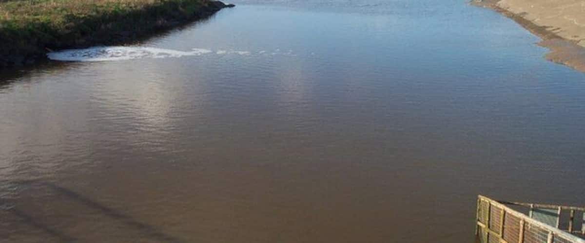 A calm river with a wooden bridge in the foreground.