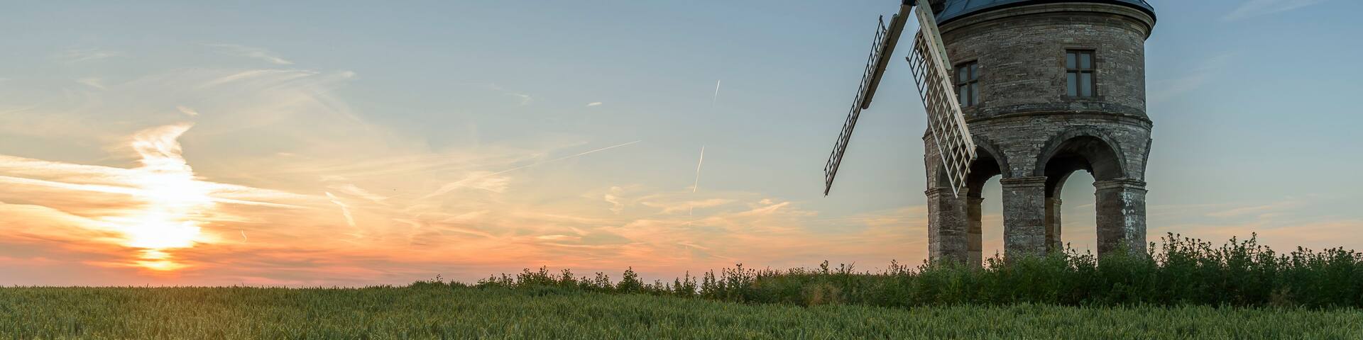 A windmill in a field with a sunset in the background.