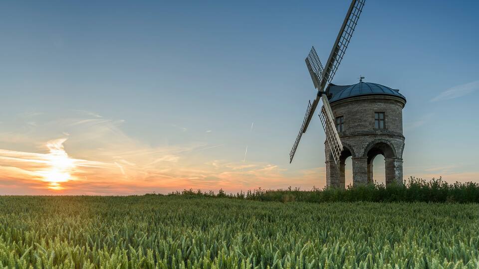 A windmill in a field with a sunset in the background.