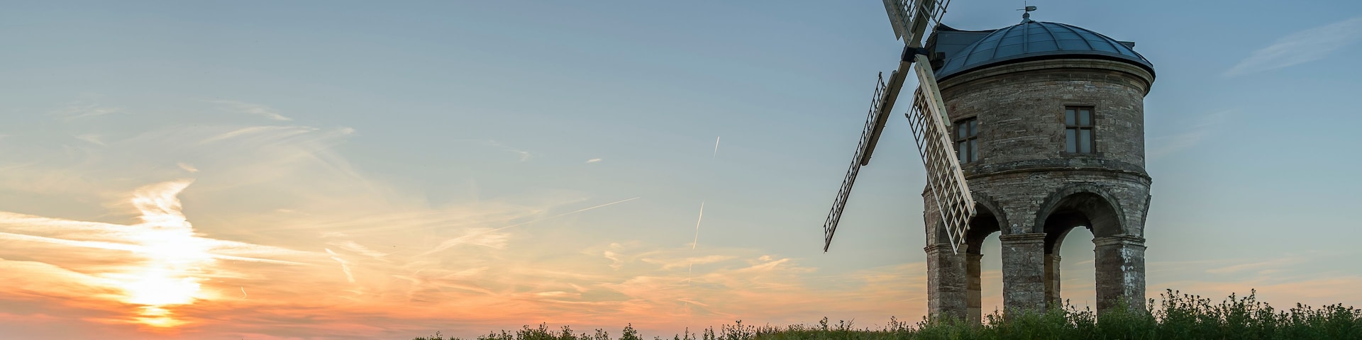 A windmill in a field with a sunset in the background.