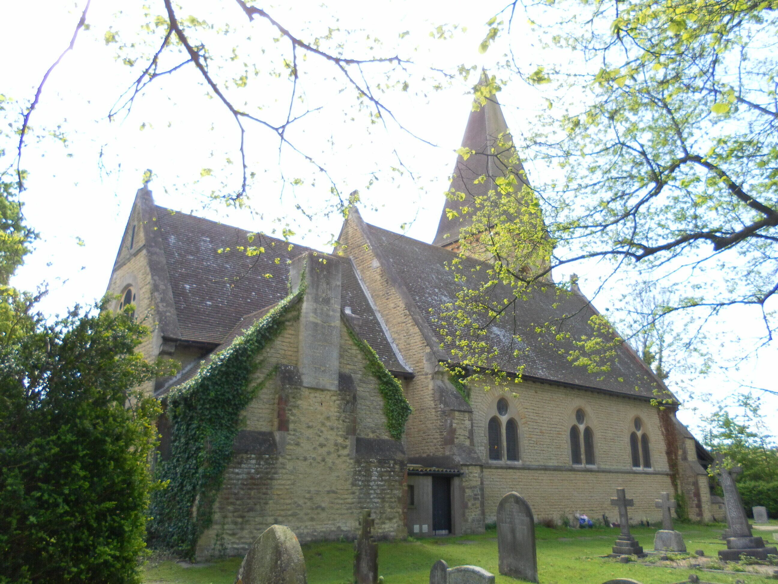 A church with a tall spire, ivy-covered walls, and a cemetery with headstones.