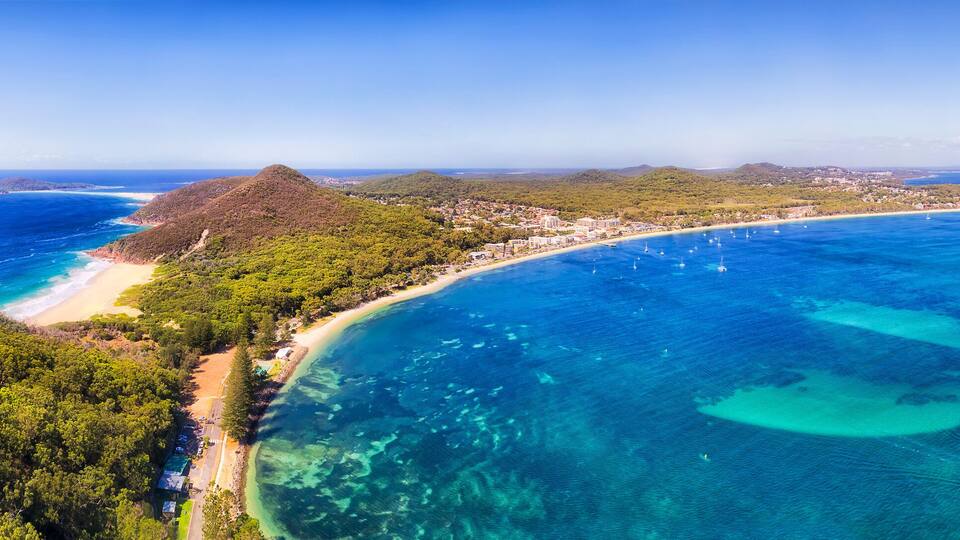 A coastal landscape with a beach, clear blue waters, and lush green hills.