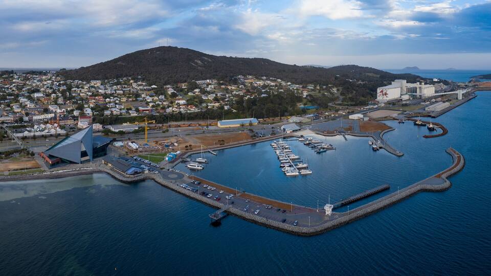 An aerial view of a coastal town with a marina, residential area, and a large industrial building.